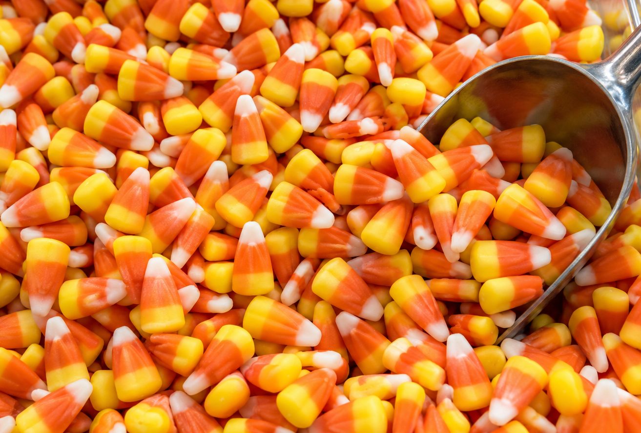 A big pile of candy corn with a metal candy scoop