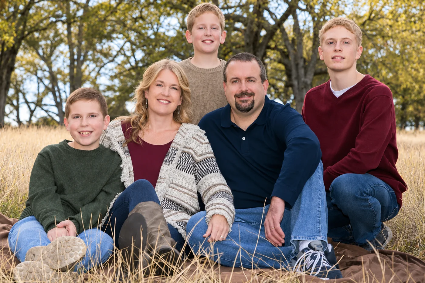 Rob and Melanie Sweeney with their three sons, sitting together in a field of golden grass